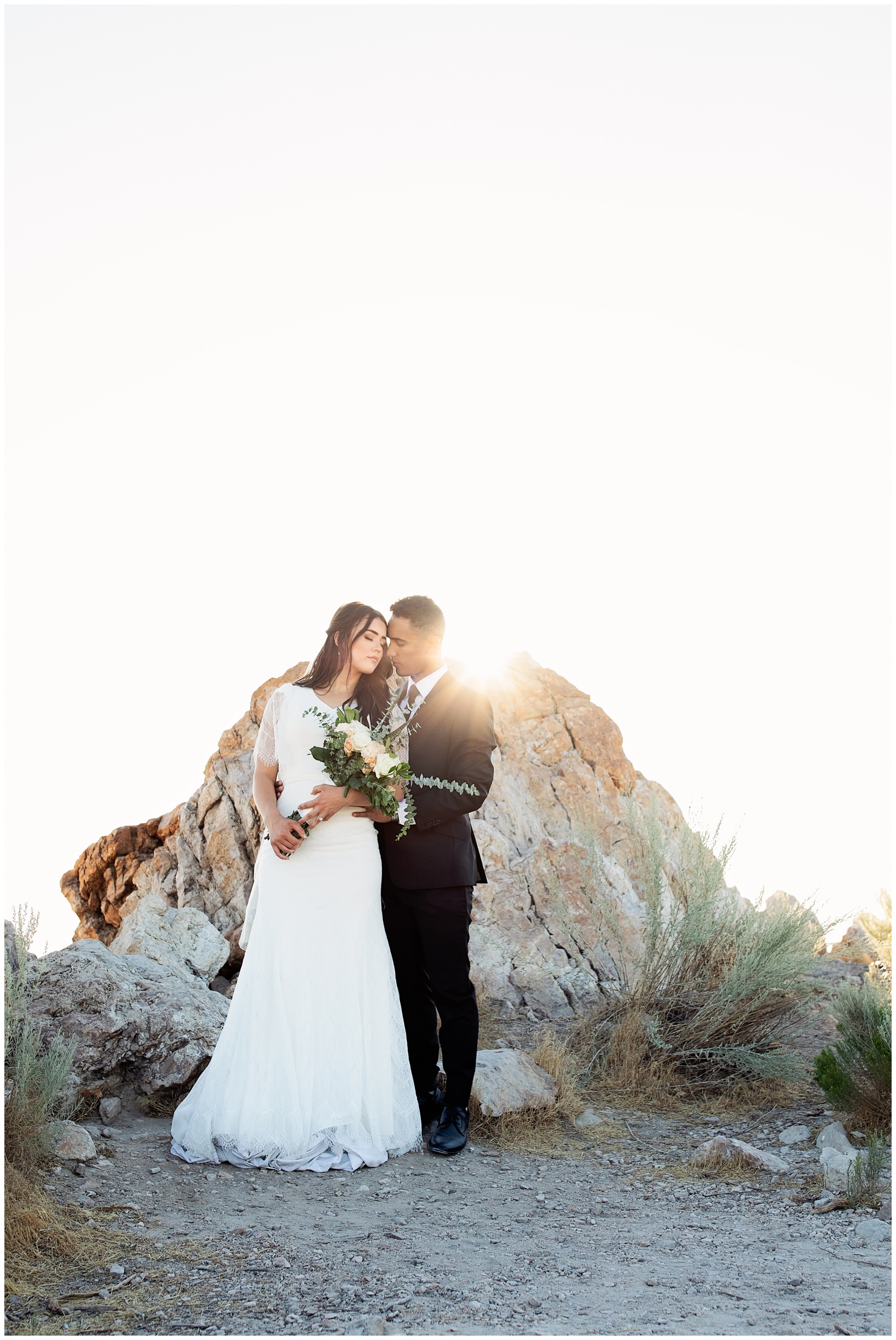 Sunburst behind the bride and groom. Groom holding onto the brides waist and snuggling close for pictures in SLC, Utah.